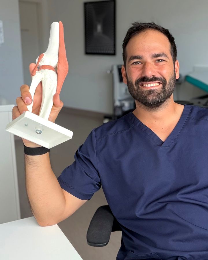 Dr. Patrik Shnawa, Facharzt für Orthopädie und Traumatologie, mit einem anatomischen Kniemodell in seiner Ordination